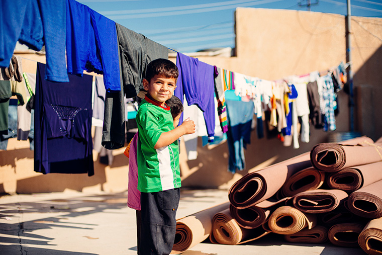 Young children, displaced by war in Iraq, play amongst rolls of carpet.