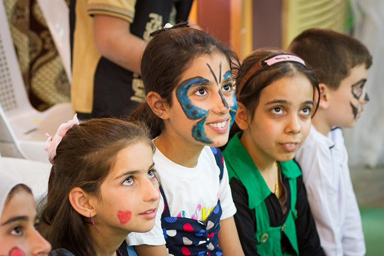 Children, their faces brightly decorated with face paint, participate in a game at an Easter party hosted by a local Assyrian church.