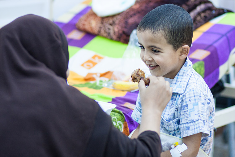Hamam's mom helps him eat his first meal after his heart surgery: spaghetti, chicken and salad.