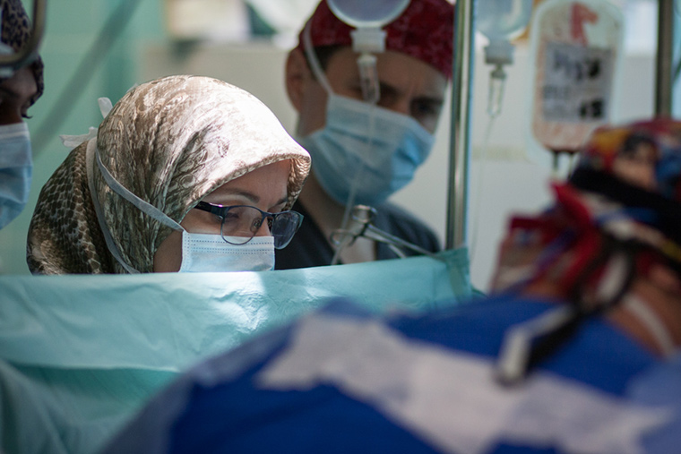 Dr. Naima peers over a screen, observing a heart surgery in progress that she diagnosed earlier.