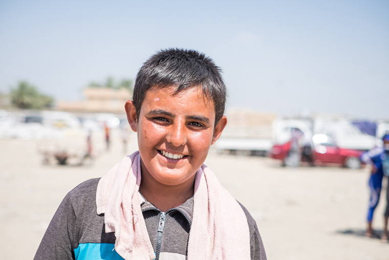 One of the boys who makes his living hauling cargo to displaced families, across the Bzebez bridge, Iraq. The heat was unbearable, he is red-faced and sweaty, but still smiles.