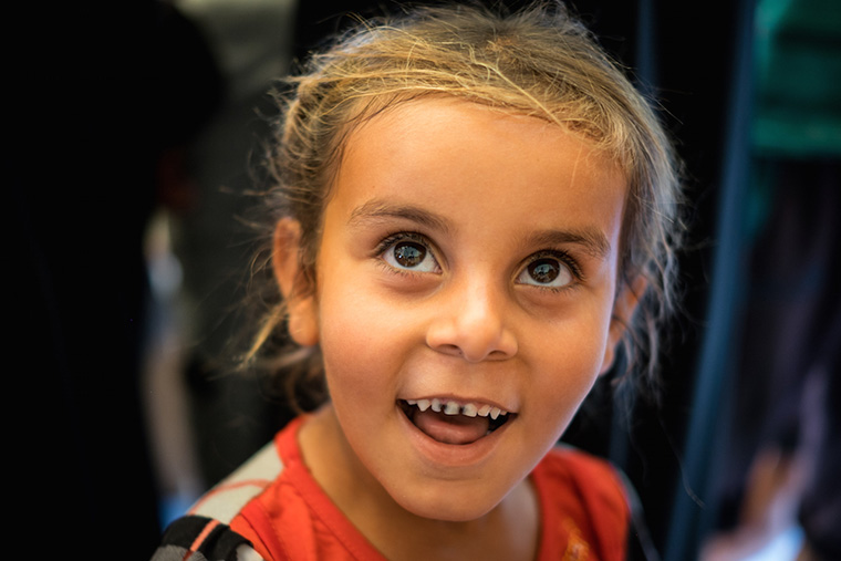 A young girl seen by a doctor during a relief aid drop. She smiles wide, revealing that her front teeth are black with cavities.