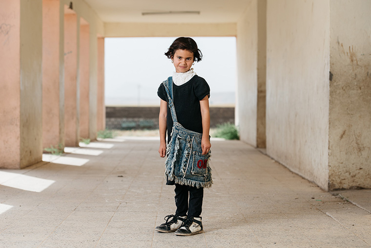 A young girl stands ready and confident to start school. Being displaced hasn't dampened her desire to learn!