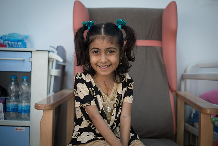 A young girl smiles, a beautiful scar across her chest, after her recent lifesaving heart surgery.