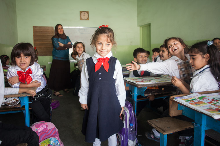 Deeya stands in her classroom, dressed in her navy uniform, surrounded by enthusiastic classmates.