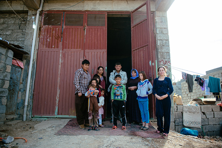Yazidi families stand outside their temporary home in a storage warehouse
