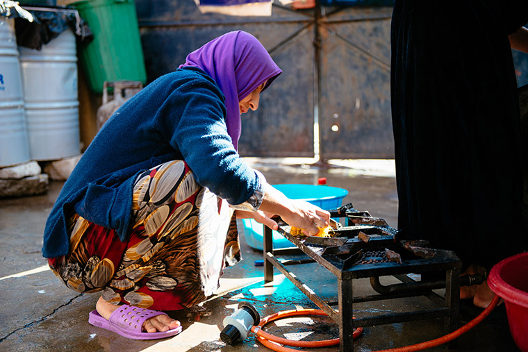 An IDP woman cleans the stove in her outdoor kitchen