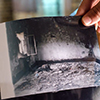 Someone holding a print photograph of a house destroyed by ISIS violence.