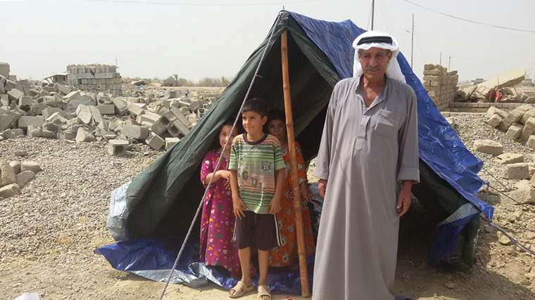 An Iraqi man and young children stand at the entrance of their new tent.