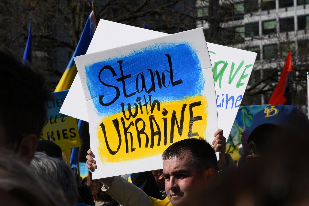 At the center of a protest in support of Ukraine, a sign is held above the crowd: Stand with Ukraine.