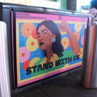 Brightly colored poster featuring the illustrated face of an AAPI woman, featuring the words "STAND WITH US"